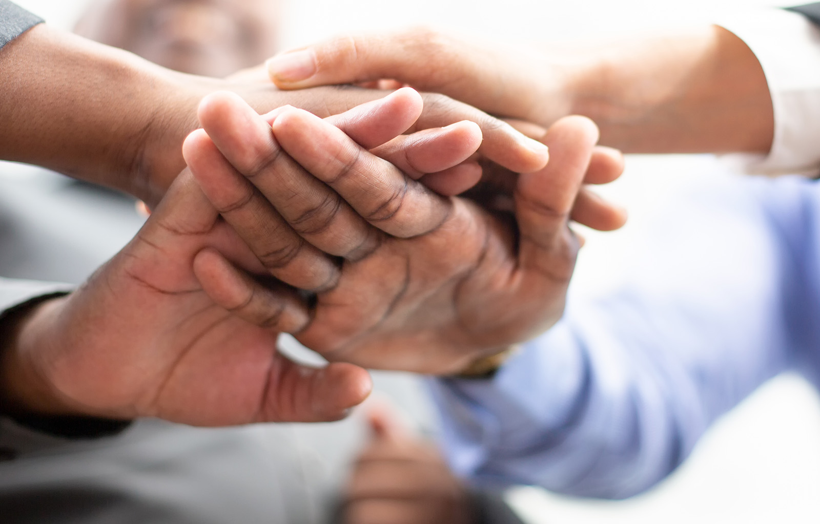 United coworkers standing with their hands together in modern office, celebrating victory, teambuilding and unity